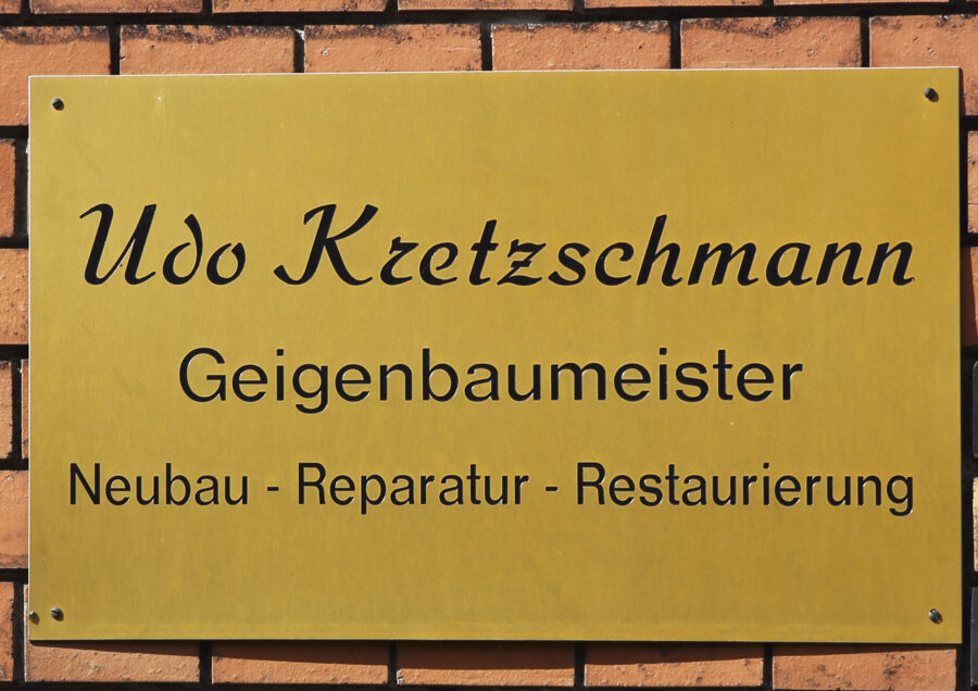 Ein gelbes Schild mit der Aufschrift "Udo Kretzschmann, Geigenbaumeister"